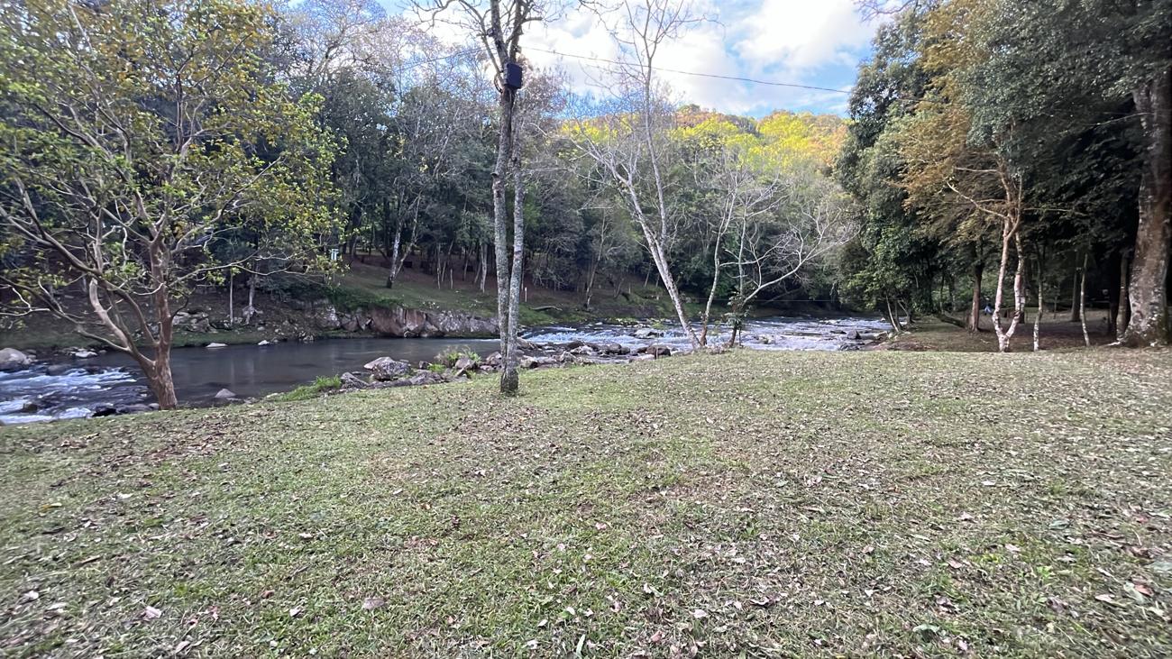 Gramado plano junto ao rio com mata ao fundo
